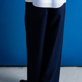 A person shown from the waist down wearing dark navy wide-leg trousers, a white shirt, and black boots, standing against a solid blue wall.