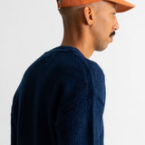 A man in profile wearing a dark navy knit sweater and an orange baseball cap, photographed against a plain white wall.