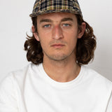 Man wearing a plaid cap and white shirt against a plain background
