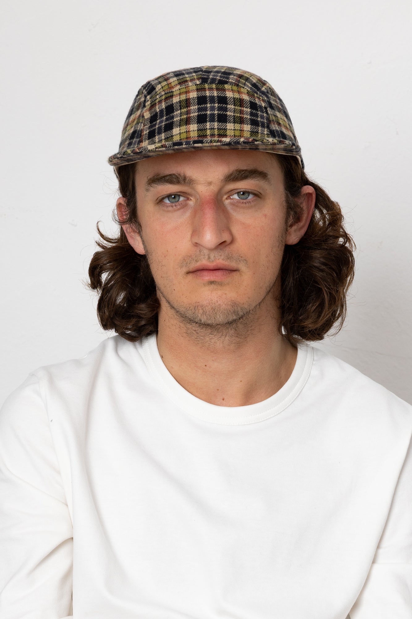 Man wearing a plaid cap and white shirt against a plain background