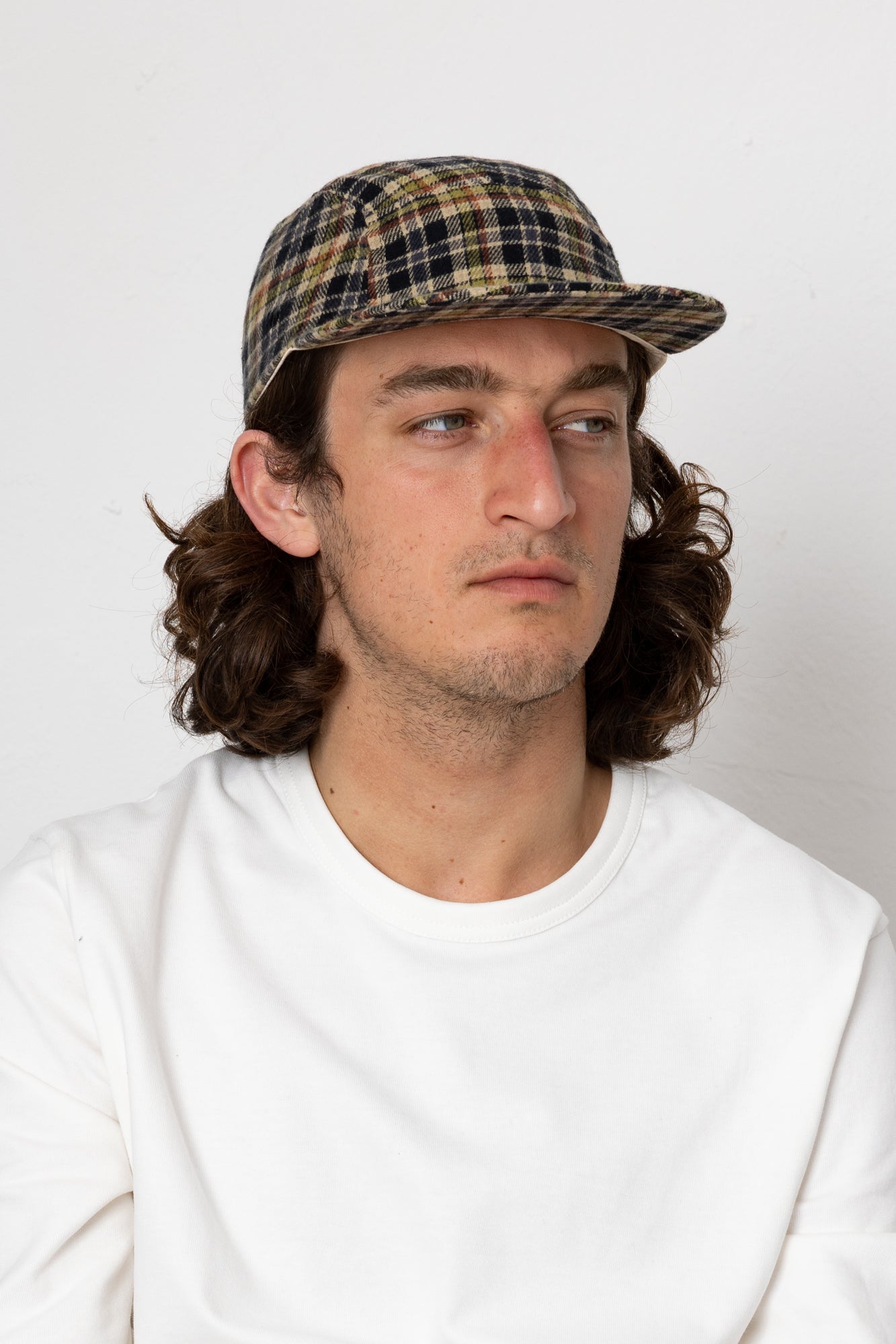 Man wearing a plaid cap and white shirt against a plain background