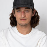 Man wearing a dark cap and white shirt against a plain background