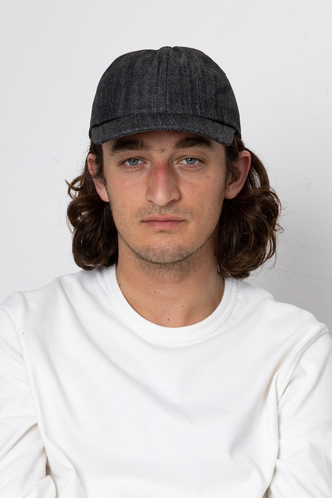 Man wearing a dark cap and white shirt against a plain background