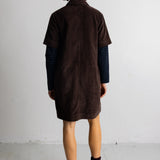 A model wearing a dark brown corduroy short-sleeve collared pullover over a blue and black striped long-sleeve shirt, set against a plain light gray background.