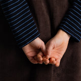 Close-up of a person's hands clasped behind a dark brown corduroy garment, with navy and blue striped sleeves visible.