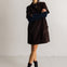A model stands in a studio wearing a dark brown corduroy mini coat over a navy and black striped long-sleeve top, paired with black ankle boots.