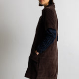 A model wearing a dark brown corduroy short-sleeve collared pullover over a blue and black striped long-sleeve shirt, set against a plain light gray background.