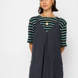 Woman wearing a striped shirt and dark gray overalls against a white background