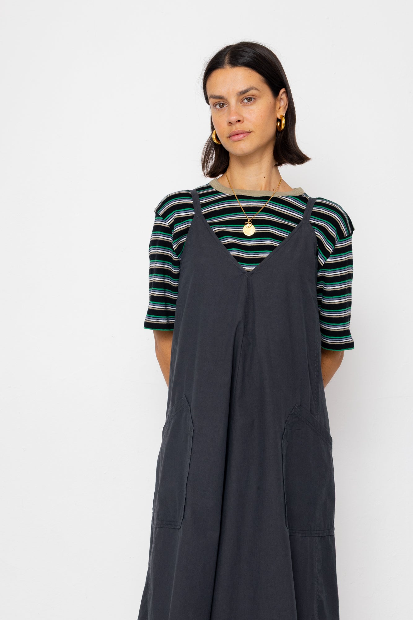 Woman wearing a striped shirt and dark gray overalls against a white background