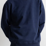 A navy blue crewneck sweatshirt worn by a model, paired with brown pants, against a plain off-white background.
