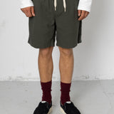 Person wearing dark green shorts, white sweatshirt, black shoes, and maroon socks against a plain background