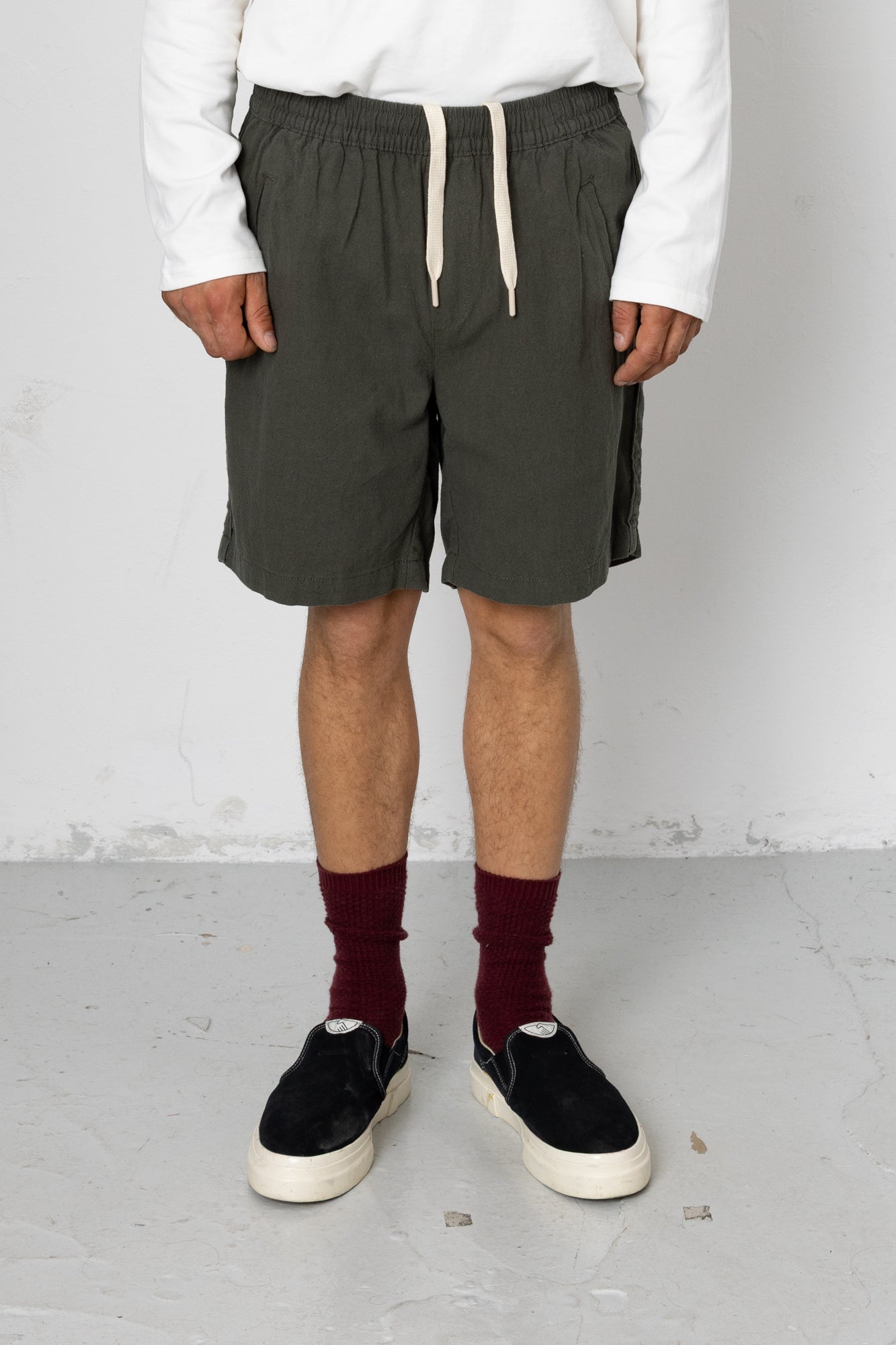 Person wearing dark green shorts, white sweatshirt, black shoes, and maroon socks against a plain background