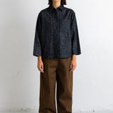 A model stands against a white wall wearing a dark navy textured long-sleeve button-up shirt and wide-leg brown trousers.