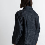 A person shown from the back wearing a dark charcoal textured overshirt and brown pants against a plain white wall.