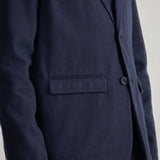 Close-up of a navy blue corduroy blazer with a single button closure and a flap pocket, worn by a model.