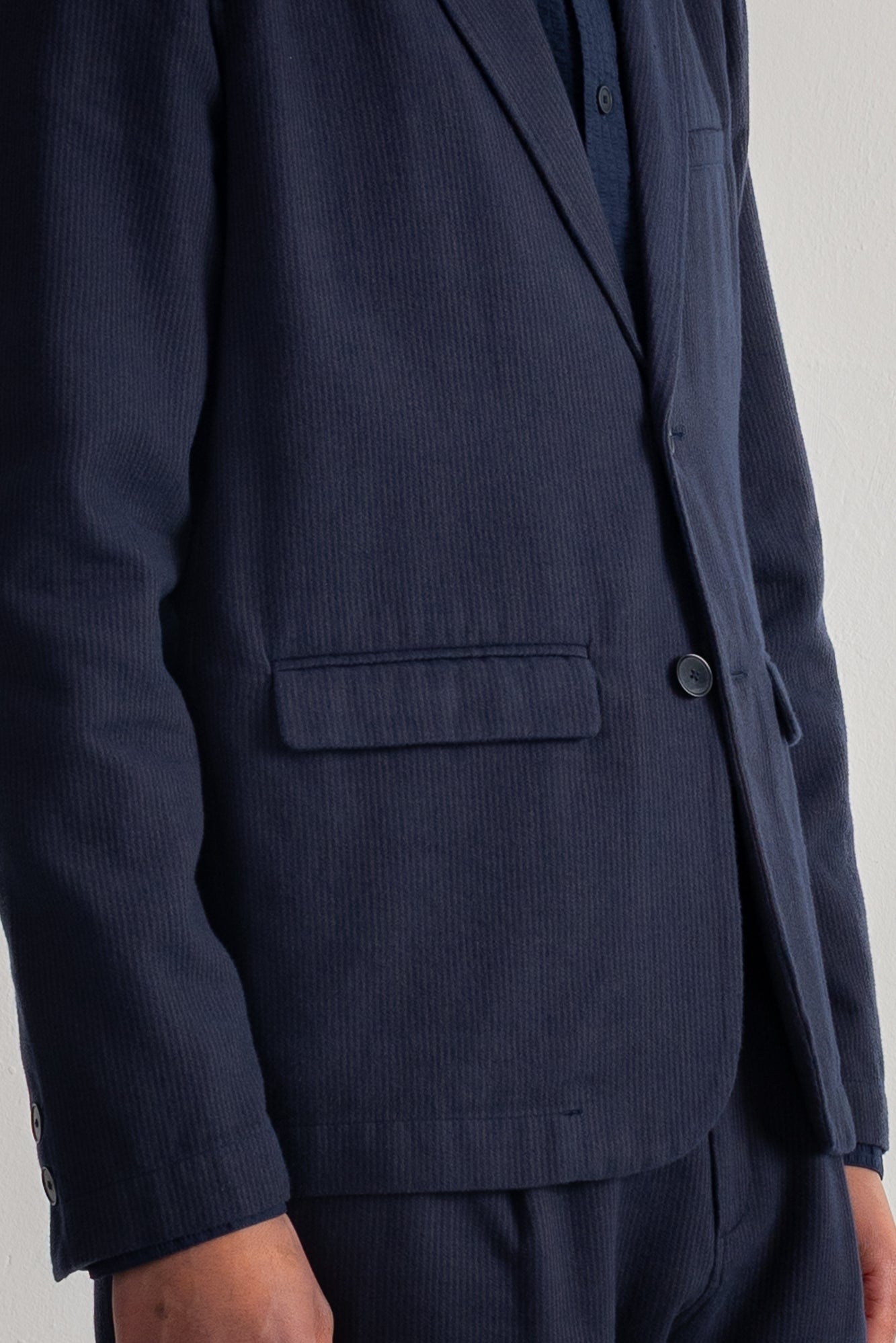 Close-up of a navy blue corduroy blazer with a single button closure and a flap pocket, worn by a model.