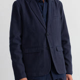 A man wearing a dark navy blue blazer over a matching navy shirt and trousers, shown from the chin down against a plain white background.