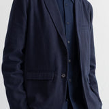 A man wearing a dark navy blue corduroy blazer over a matching navy shirt, shown from the neck down against a plain light background.
