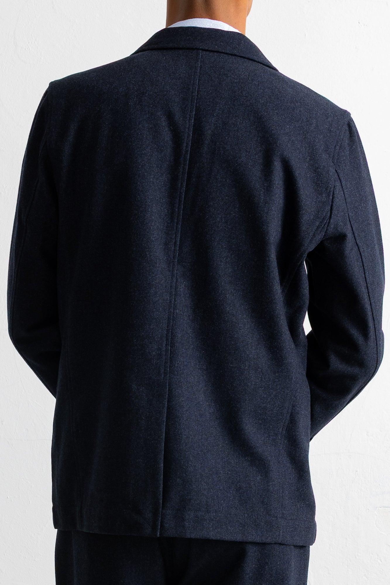 Back view of a person wearing a dark navy blazer over a white collared shirt, shown against a plain light background.