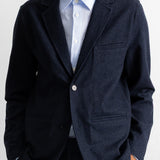 A man wearing a dark navy blue textured blazer over a light blue striped dress shirt, shown from the chin down against a plain white background.