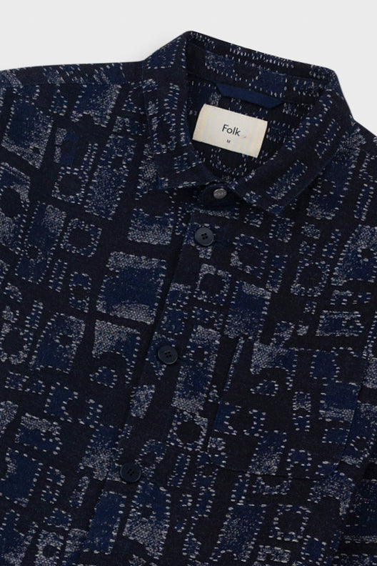 Close-up of a dark blue patterned shirt with a brand label on a light gray background