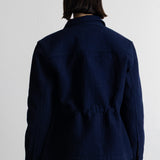 A person shown from the back wearing a dark navy blue textured jacket and brown pants against a plain white wall.