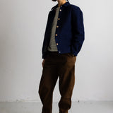 A model stands against a white studio wall wearing a navy blue button-up jacket over a gray and white striped shirt, paired with brown corduroy pants and beige lace-up boots.