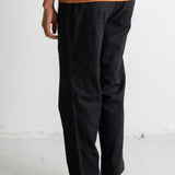 A person shown from the waist down wearing loose black pants, an orange t-shirt, and black Converse high-top sneakers against a white wall.