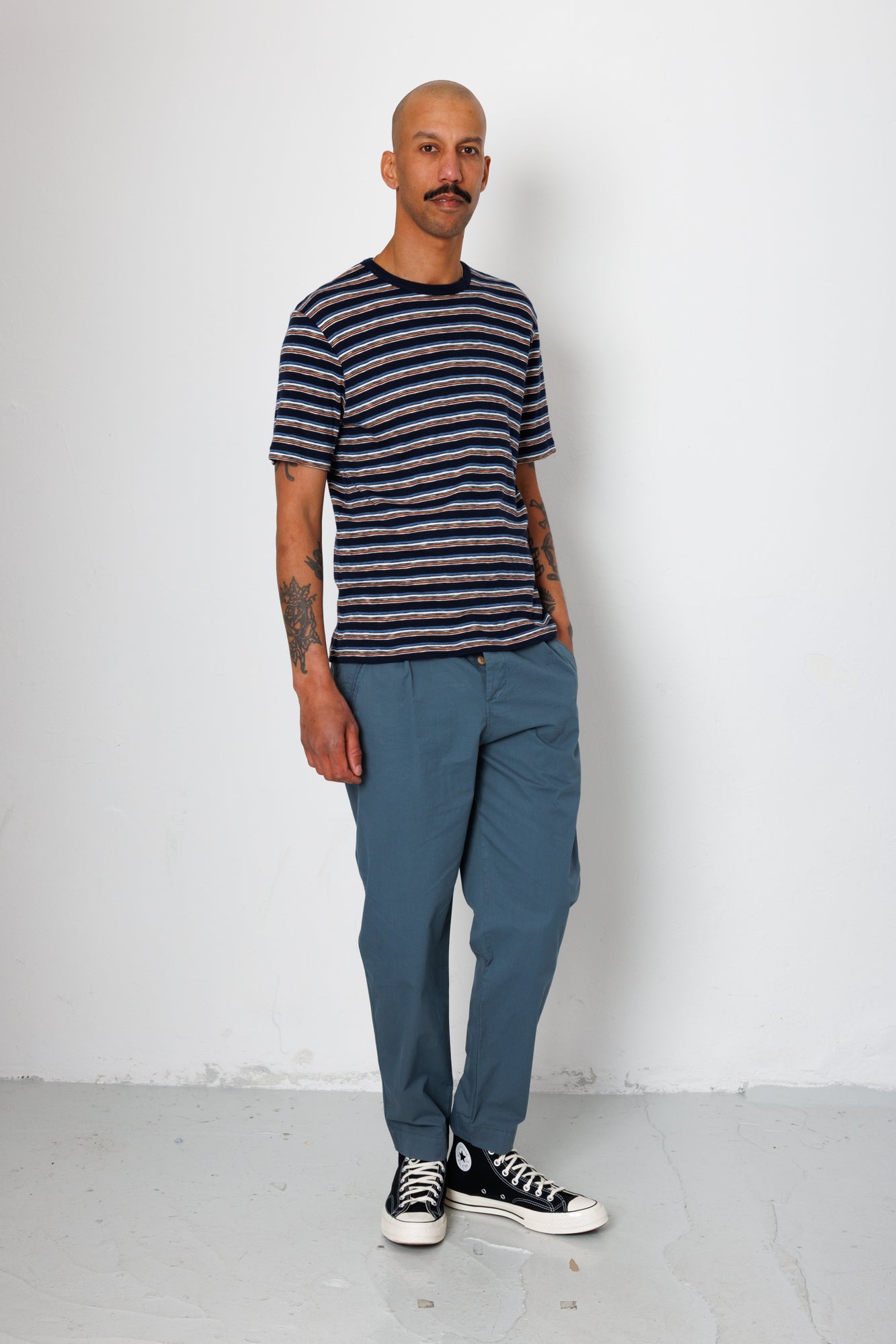 Man wearing a striped shirt, blue pants, and black sneakers against a white background