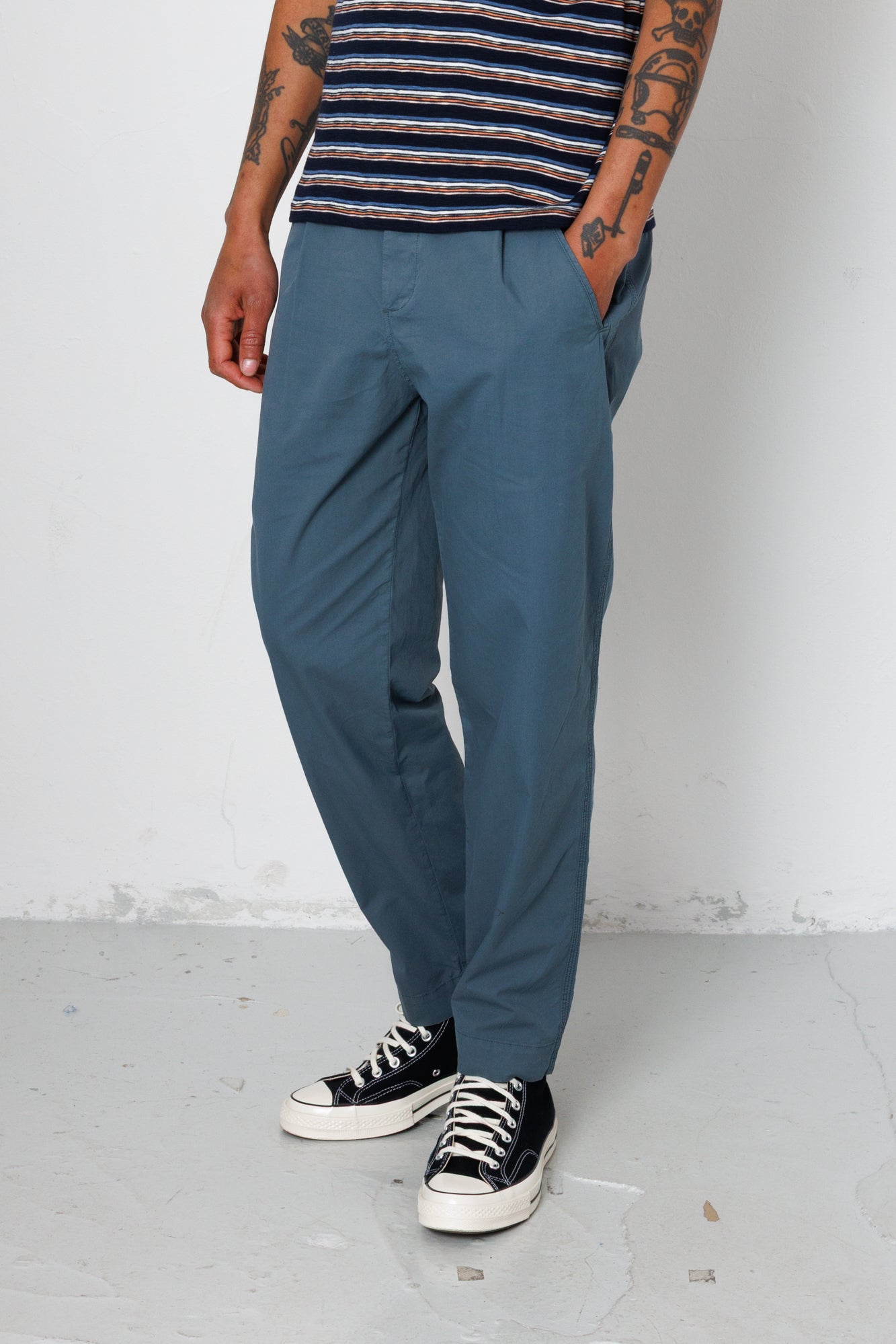 Person wearing blue pants and a striped shirt with black sneakers on a plain background