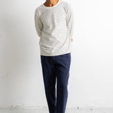 A man wearing a cream and navy striped long-sleeve shirt, navy pants, and black canvas sneakers, standing against a white wall.