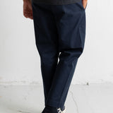 A person wearing dark navy trousers, a dark striped t-shirt, and navy high-top sneakers with white soles, standing against a white wall.