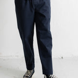 A person wearing dark navy pants, a dark striped shirt, and black canvas sneakers with white soles, standing against a light gray wall.