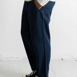 A person wearing dark navy wide-leg trousers, a cream and navy striped long-sleeve shirt, and navy canvas sneakers with white rubber soles, standing against a white wall.