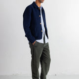 A man wearing a navy blue button-up cardigan over a white shirt, olive green pants, and black sneakers with yellow laces, standing against a white studio wall.
