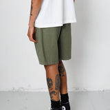 Person wearing green shorts, a white shirt, black socks, and black sneakers on a plain background