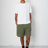 Man wearing a white t-shirt and green shorts standing against a white background