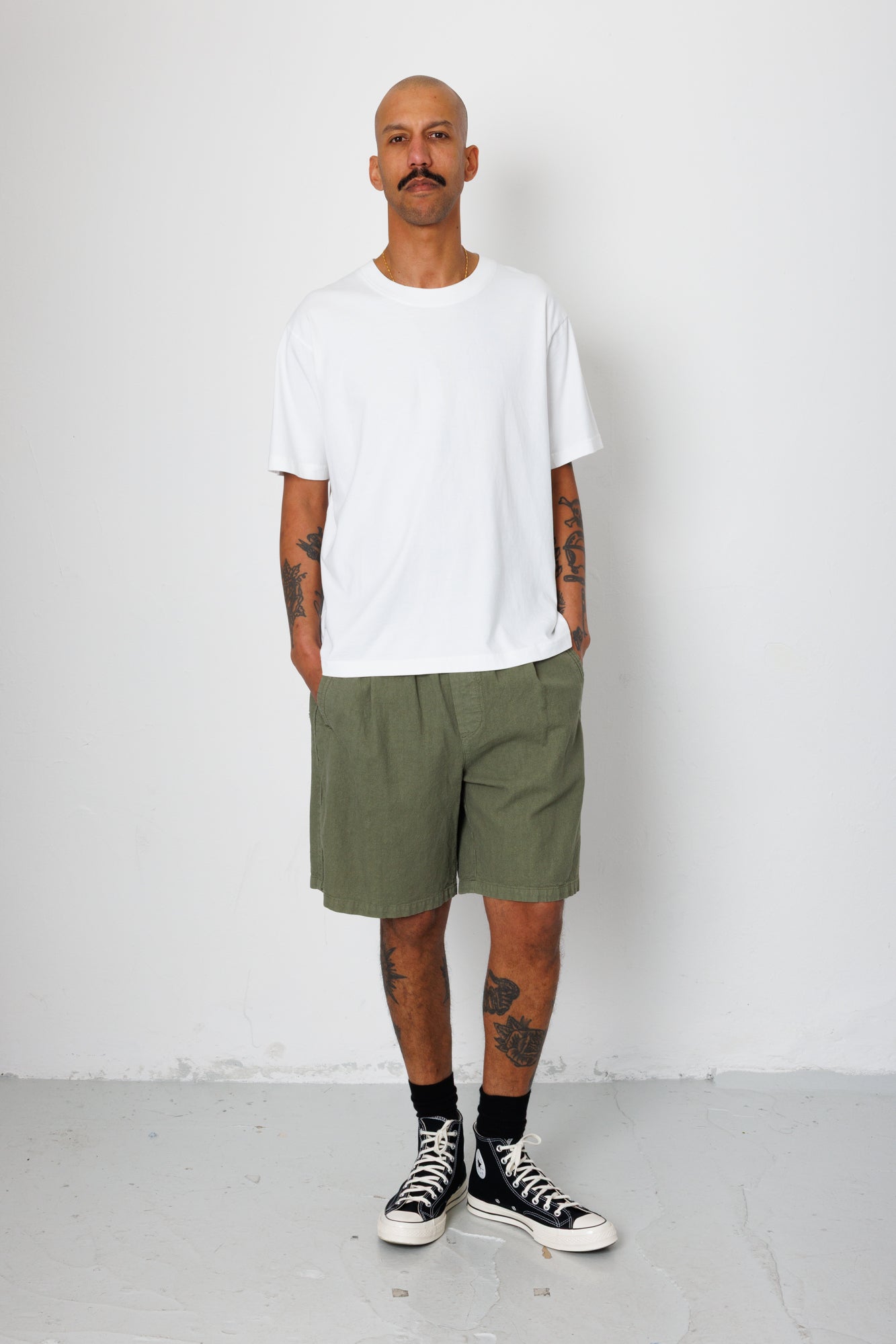 Man wearing a white t-shirt and green shorts standing against a white background