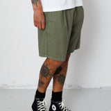 Person wearing olive green shorts, black high-top sneakers, and white socks on a plain background