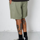 Person wearing olive green shorts, black socks, and black sneakers on a white background