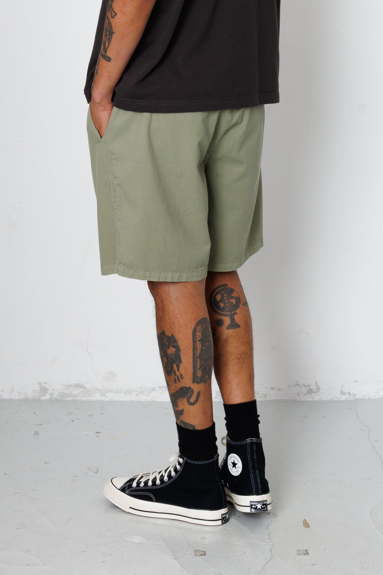 Person wearing olive green shorts, black socks, and black sneakers on a white background