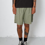 Person wearing a black t-shirt, green shorts, and black sneakers with white soles on a plain background.