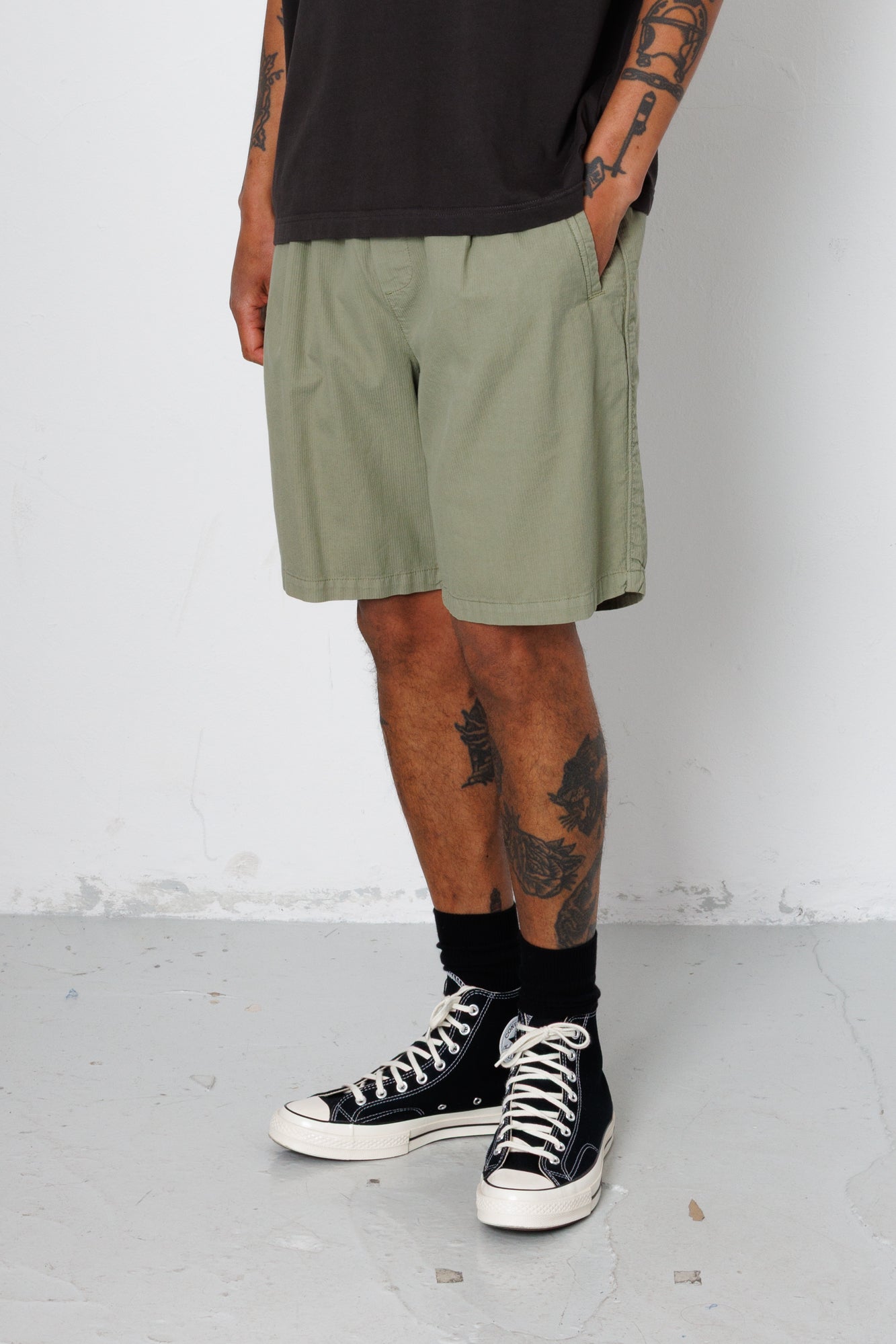Person wearing green shorts and black high-top sneakers on a white background