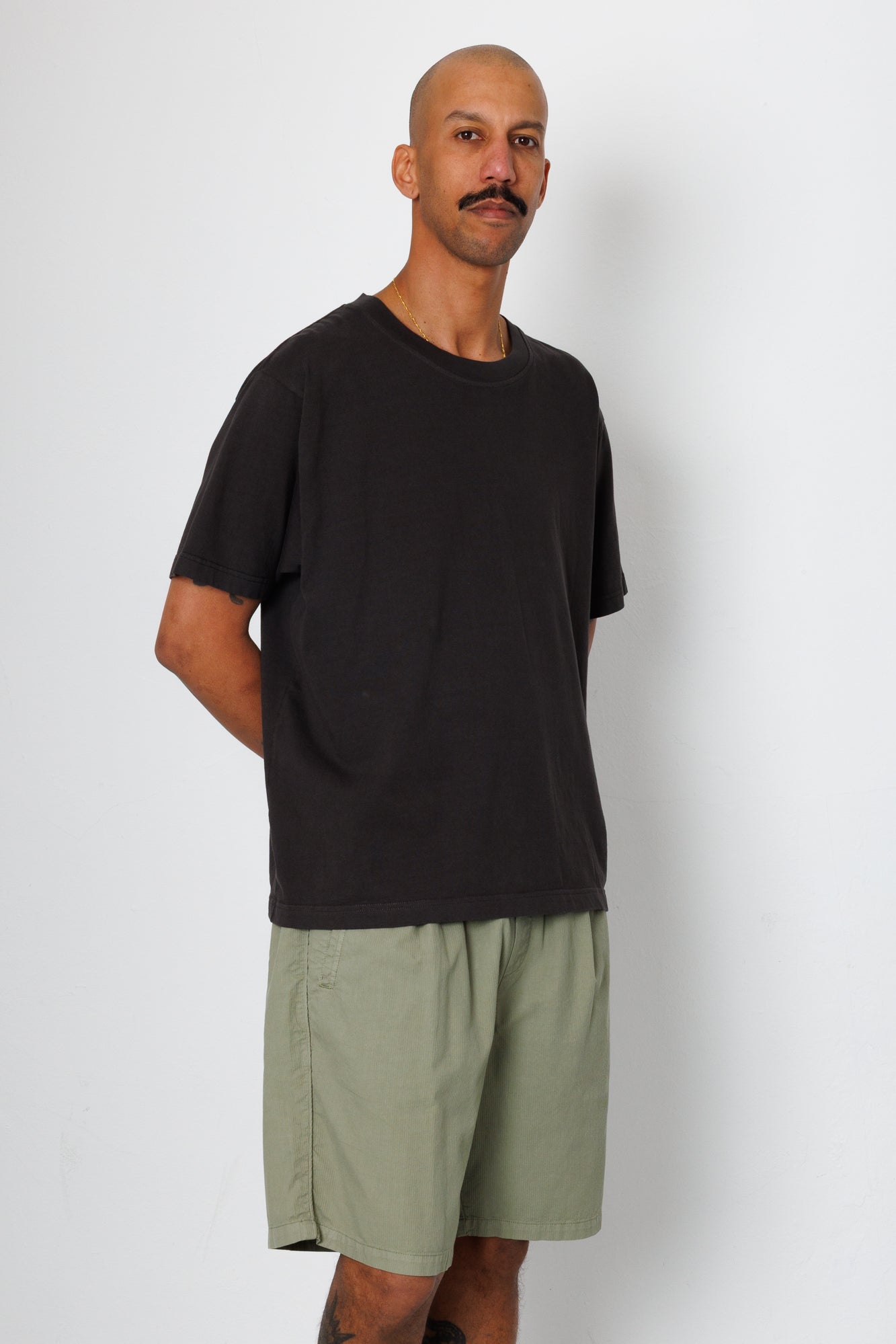 Man wearing a black t-shirt and green shorts against a white background
