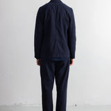 A man viewed from behind wearing a dark navy blue jacket and matching navy trousers, standing against a plain white wall.