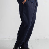 A person wearing dark navy trousers and black leather loafers, shown from the waist down against a light gray wall and floor.