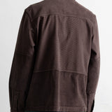 A man viewed from the back wearing a dark brown corduroy jacket and teal-green pants against a plain white background.