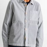 A man wearing a light gray corduroy button-up overshirt with a chest pocket and two large front patch pockets, paired with dark blue jeans.