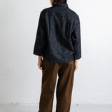 A model shown from the back wearing a dark navy textured long-sleeve shirt and brown wide-leg trousers, standing against a plain white wall.