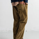 A person wearing brown corduroy pants with a navy shirt and black shoes, standing against a white wall.